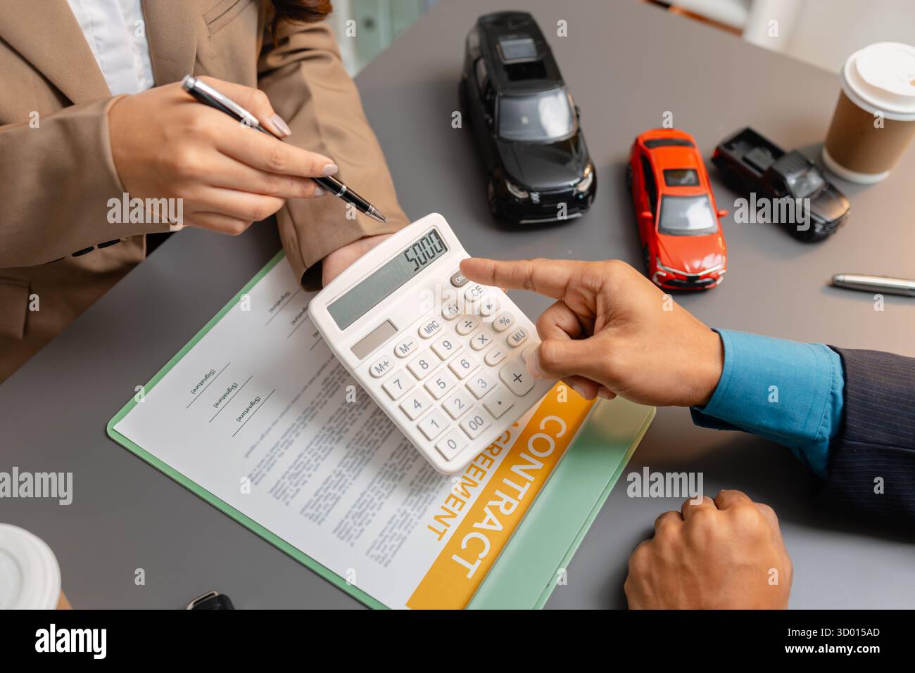 Un uomo d'affari e un cliente stanno esaminando e firmando un contratto di vendita di auto presso una scrivania, con modellini di auto di piccole dimensioni, una tazza di caffè e documenti intorno a loro, Foto Stock