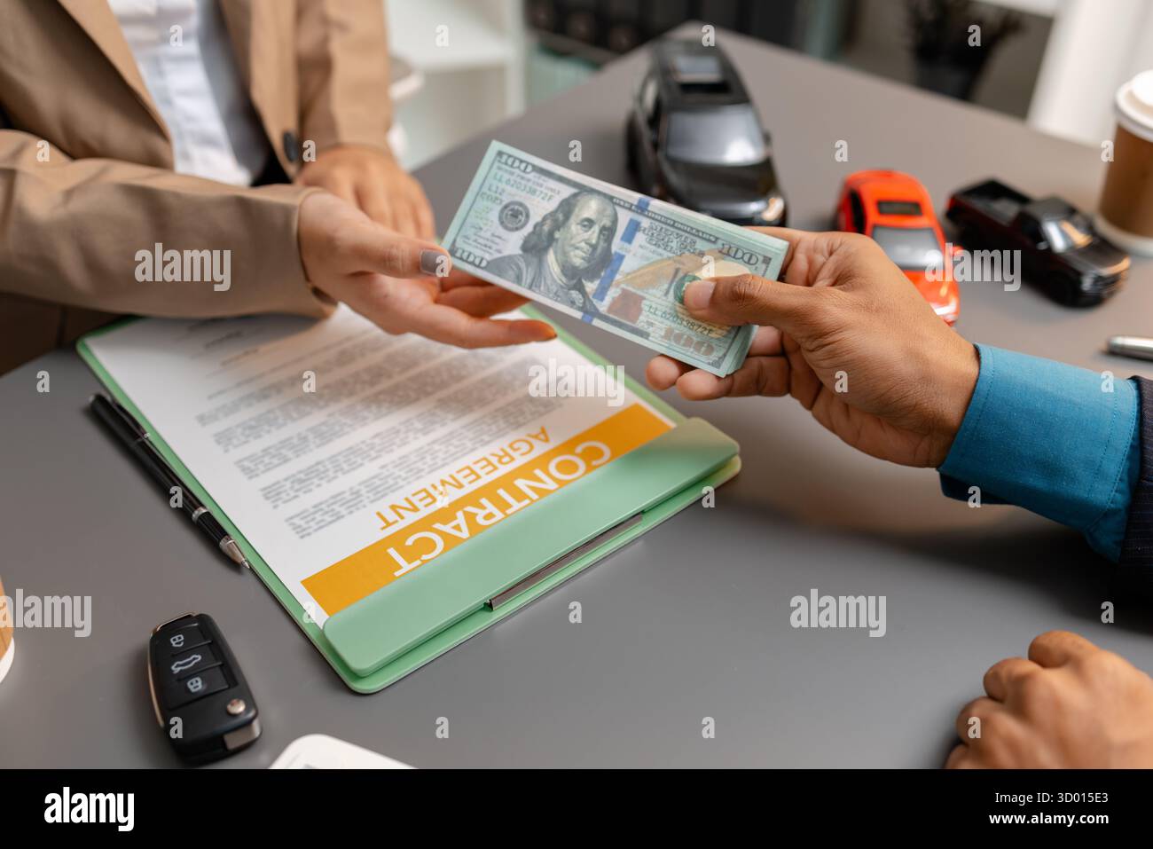 Un uomo d'affari e un cliente stanno esaminando e firmando un contratto di vendita di auto presso una scrivania, con modellini di auto di piccole dimensioni, una tazza di caffè e documenti intorno a loro, Foto Stock