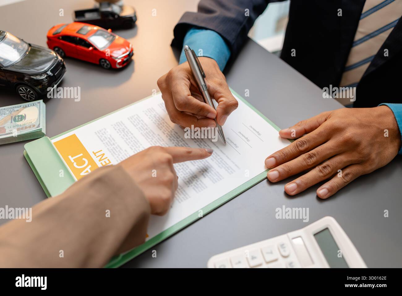 Un uomo d'affari e un cliente stanno esaminando e firmando un contratto di vendita di auto presso una scrivania, con modellini di auto di piccole dimensioni, una tazza di caffè e documenti intorno a loro, Foto Stock