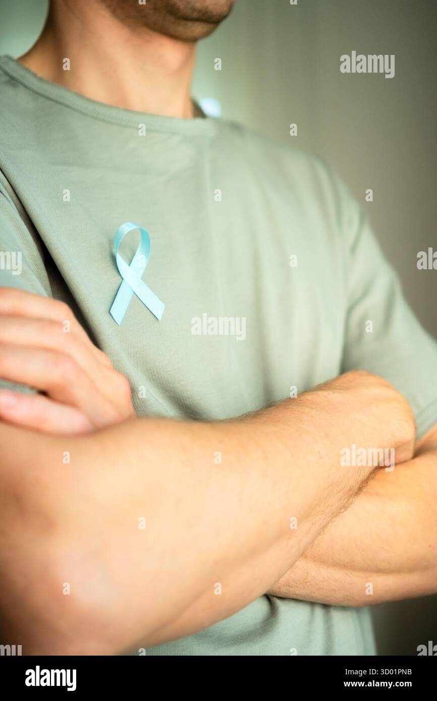Primo piano di un uomo con nastro in raso blu sulla camicia e braccia incrociate. Simbolo del mese di consapevolezza del cancro alla prostata a novembre, autocontrollo, diagnosi e trattamento medico tempestivo. Foto Stock