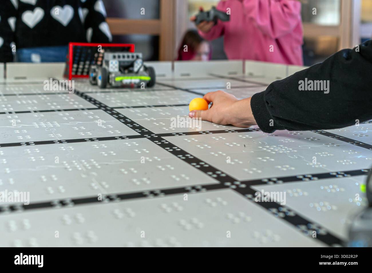 Durante un evento tecnologico, i partecipanti si confrontano con robot e una palla su una superficie di apprendimento tattile. Foto Stock