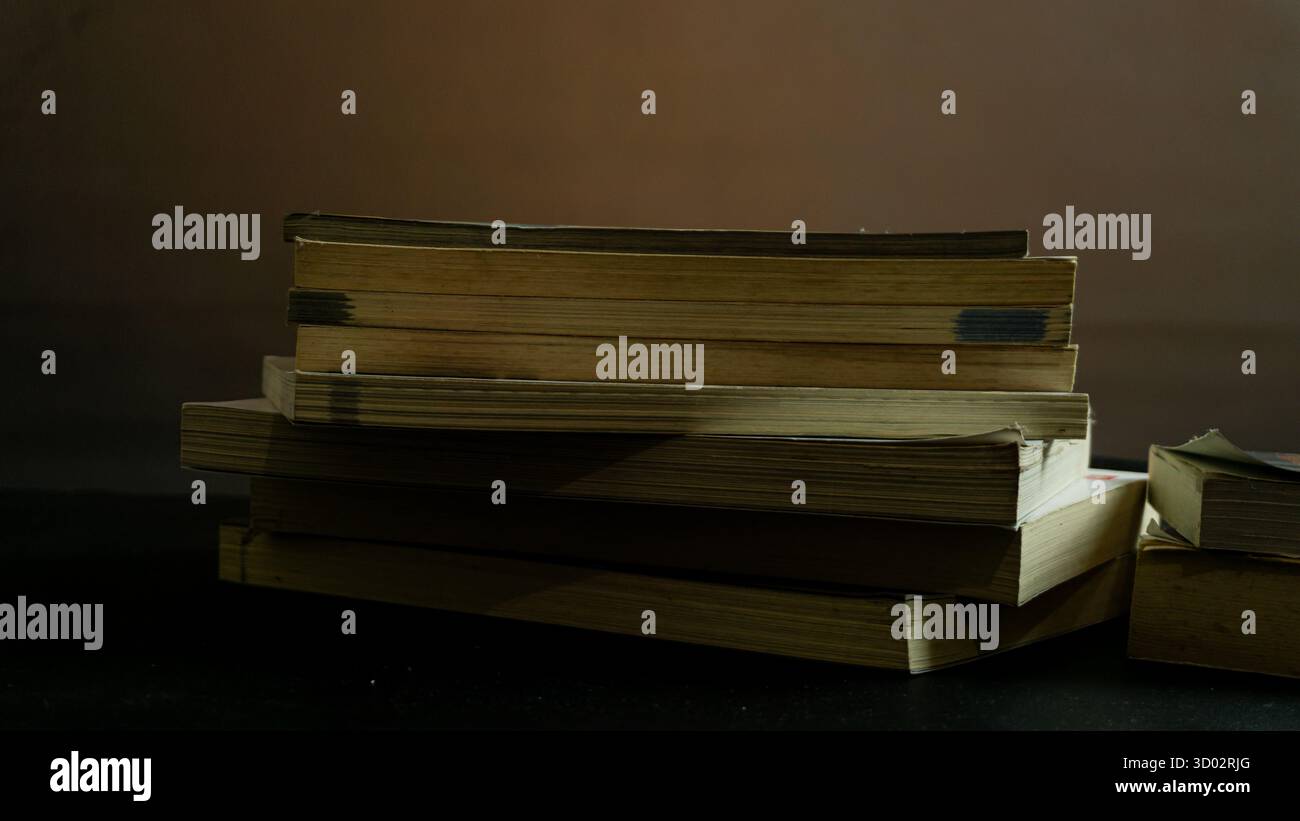 Due pile di libri su sfondo nero sotto una calda luce ambientale, una scena accogliente e intellettuale con ombre tenui e un'atmosfera soffusa Foto Stock