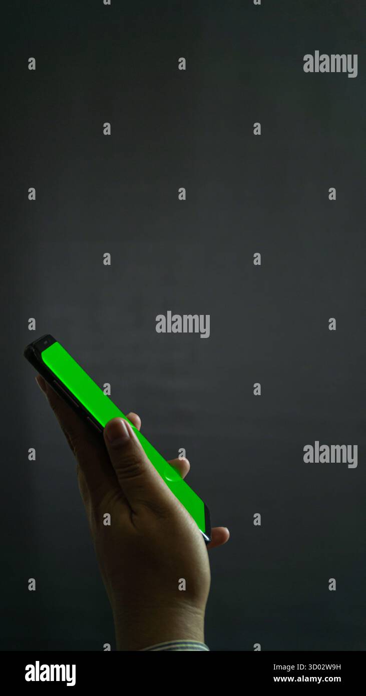 Smartphone con mano sinistra con schermo verde leggermente inclinato lateralmente, sfondo nero per un mockup pulito e utilizzo della progettazione dell'interfaccia utente Foto Stock