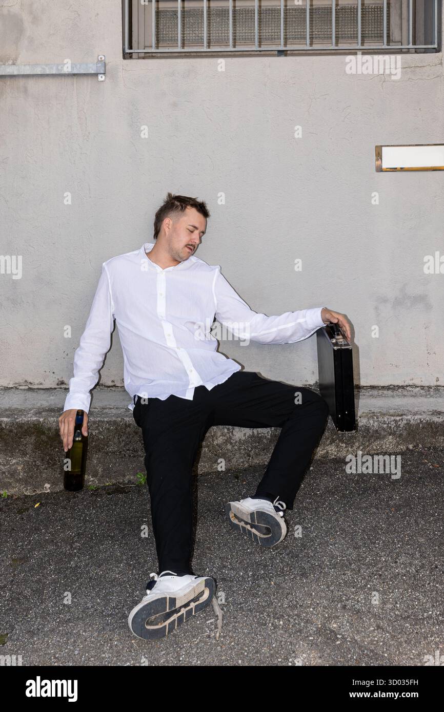 Un giovane che indossa una camicia bianca dorme completamente ubriaco per terra in strada. Problemi dei giovani uomini d'affari. Foto Stock