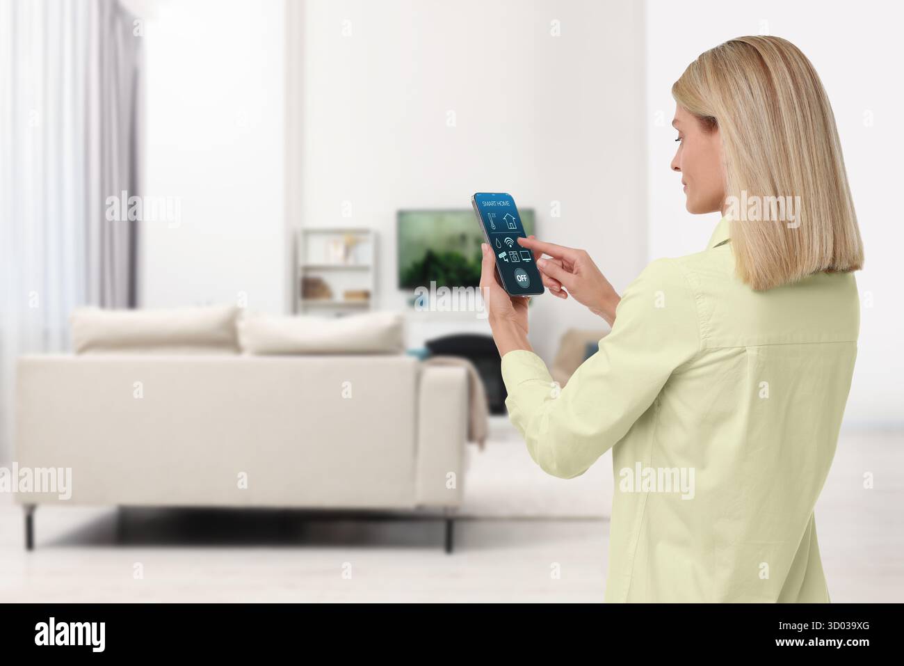 Donna che utilizza un'app per la casa intelligente sul telefono cellulare per controllare le funzioni della casa Foto Stock