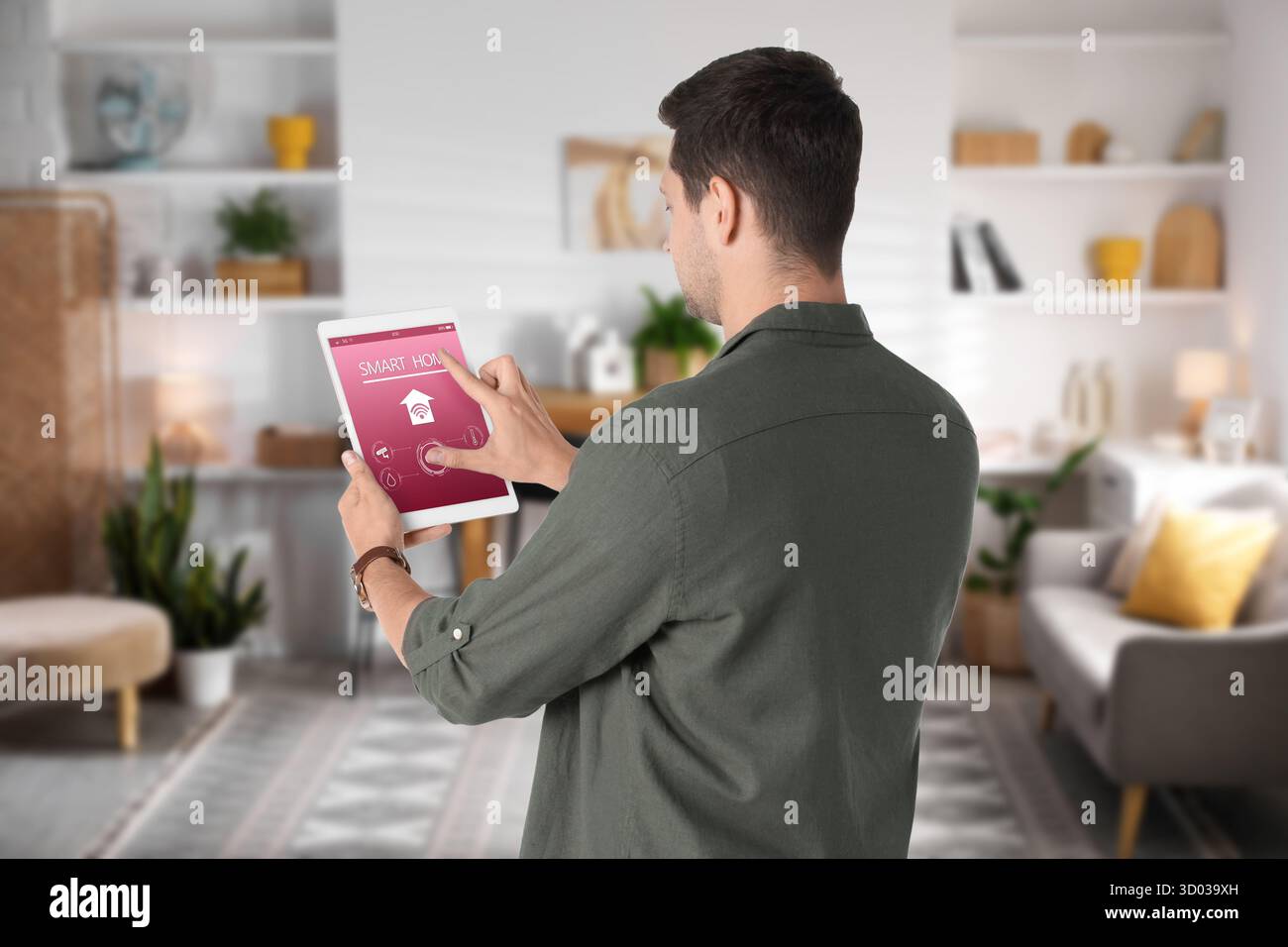 Uomo che utilizza un'app smart home su un tablet per controllare le funzionalità della casa Foto Stock