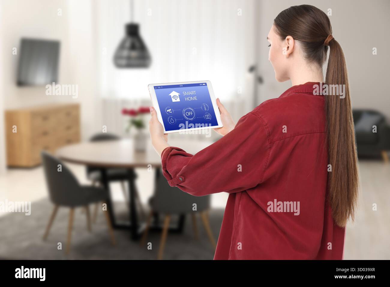 Donna che utilizza un'app per la casa intelligente su un tablet per controllare le funzionalità della casa Foto Stock