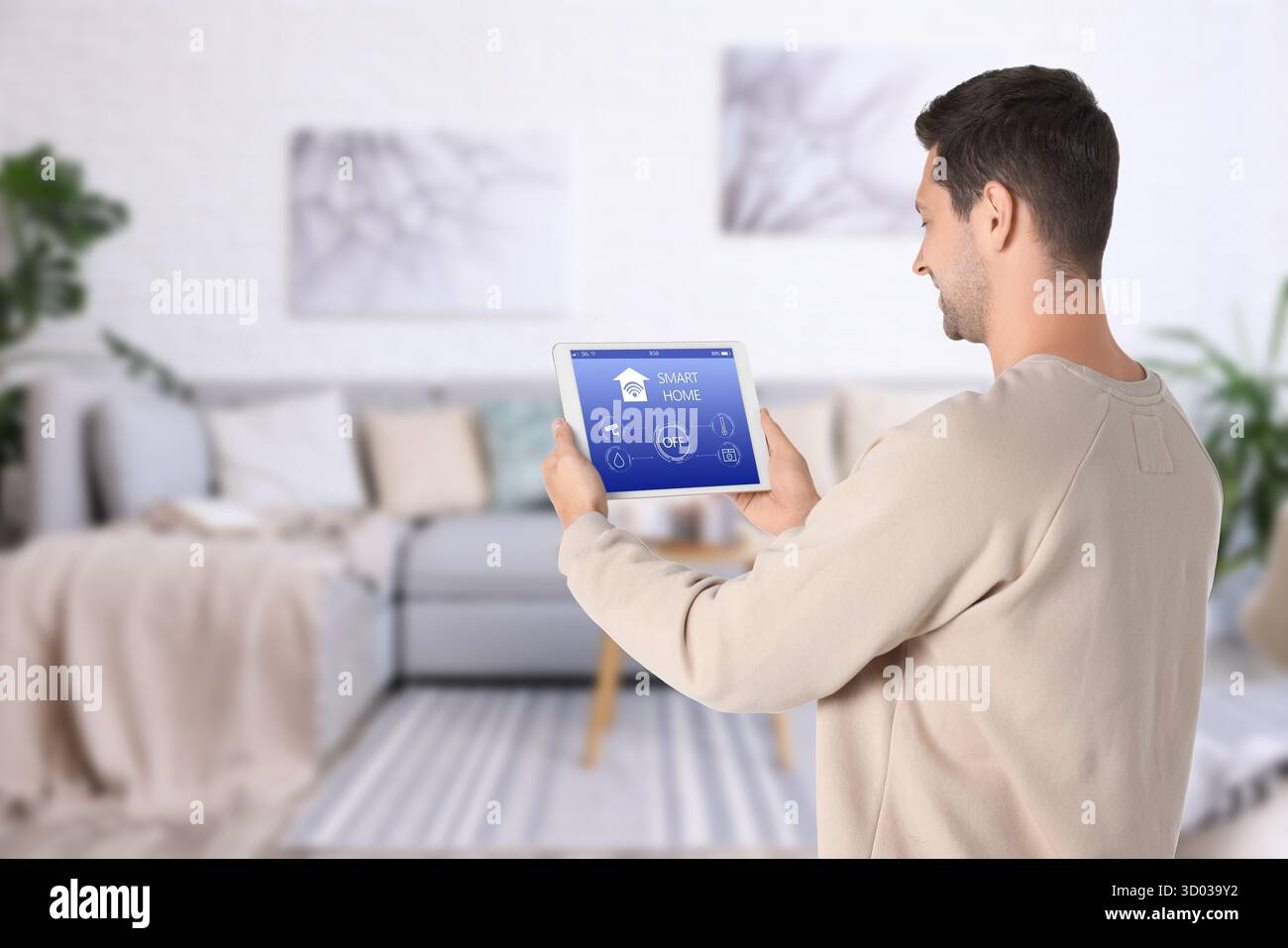 Uomo che utilizza un'app smart home su un tablet per controllare le funzionalità della casa Foto Stock