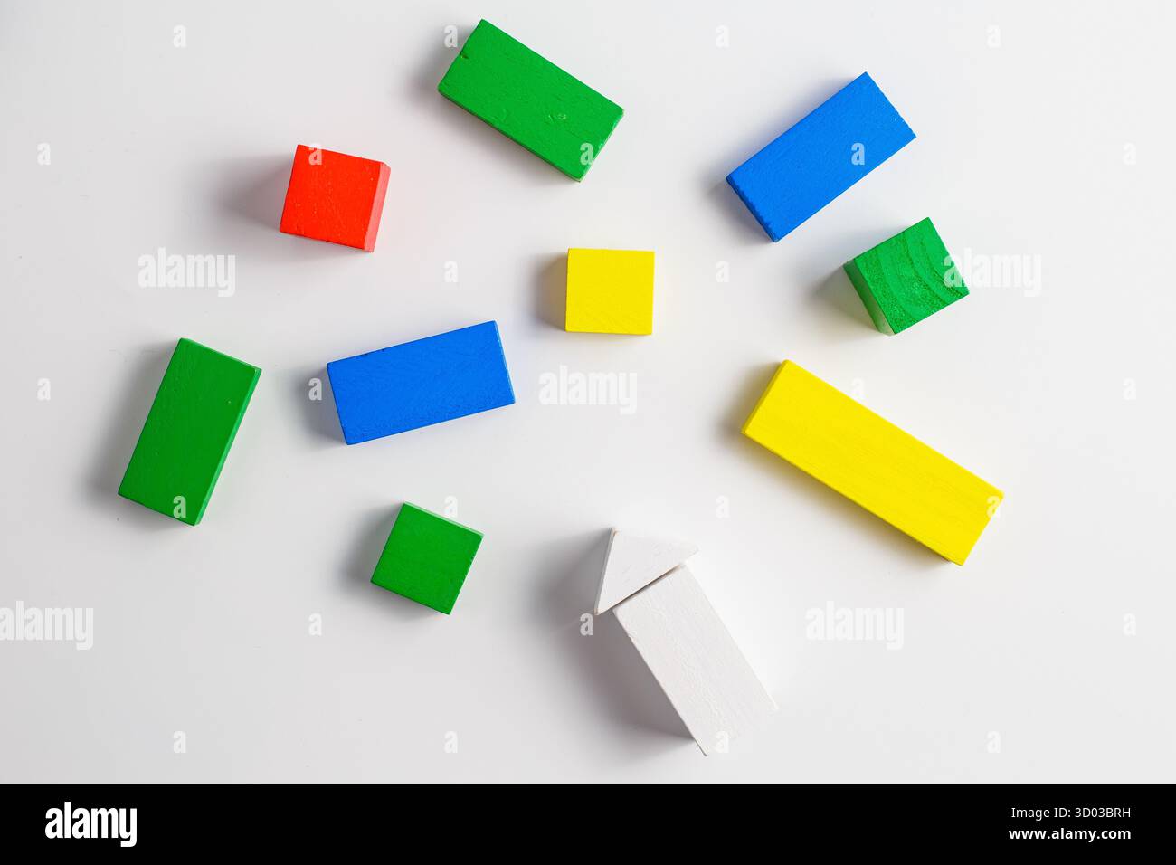 Diversi blocchi di legno colorati in varie forme, tra cui rettangoli, quadrati e una freccia bianca, disposti in modo casuale su uno sfondo bianco pulito. Foto Stock