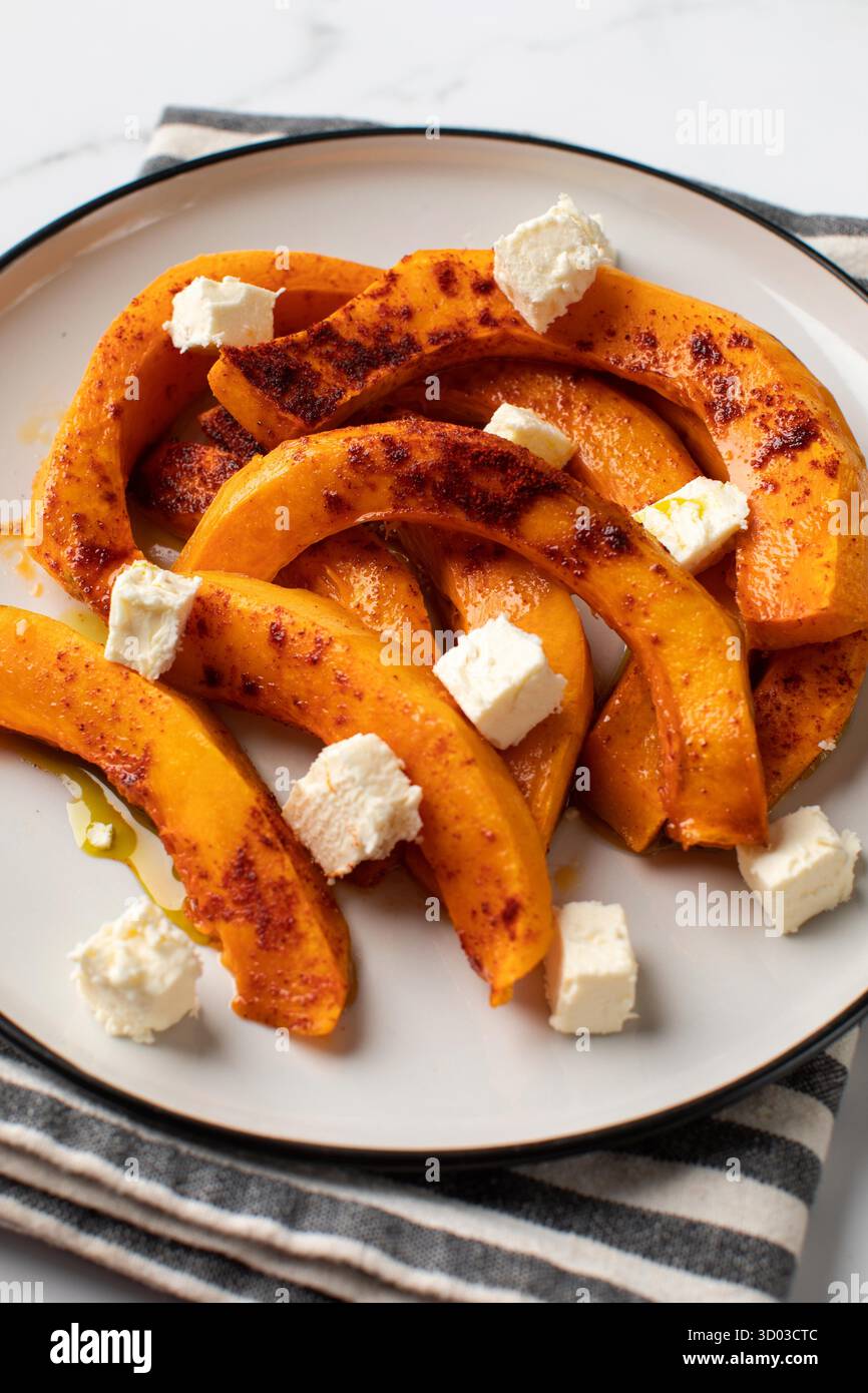 Fette di zucca al forno con spezie e cubetti di feta. Ricette autunnali, piatti di zucca. Foto Stock