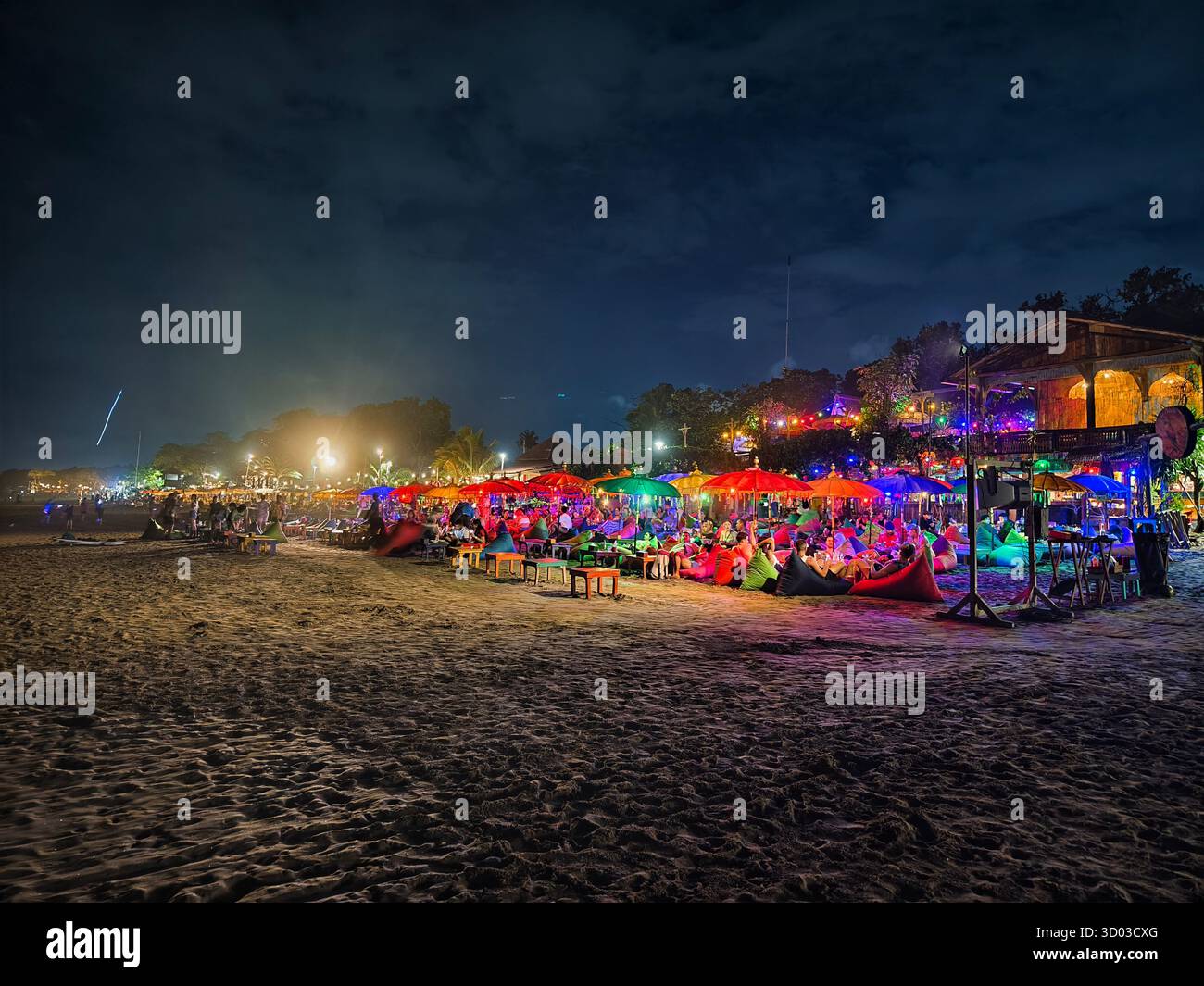 Seminyak, Bali, Indonesia – 19 ottobre 2025: Fotografia notturna di un bar caffetteria sulla spiaggia con ombrelloni colorati, borse di fagioli e luci per i turisti Foto Stock