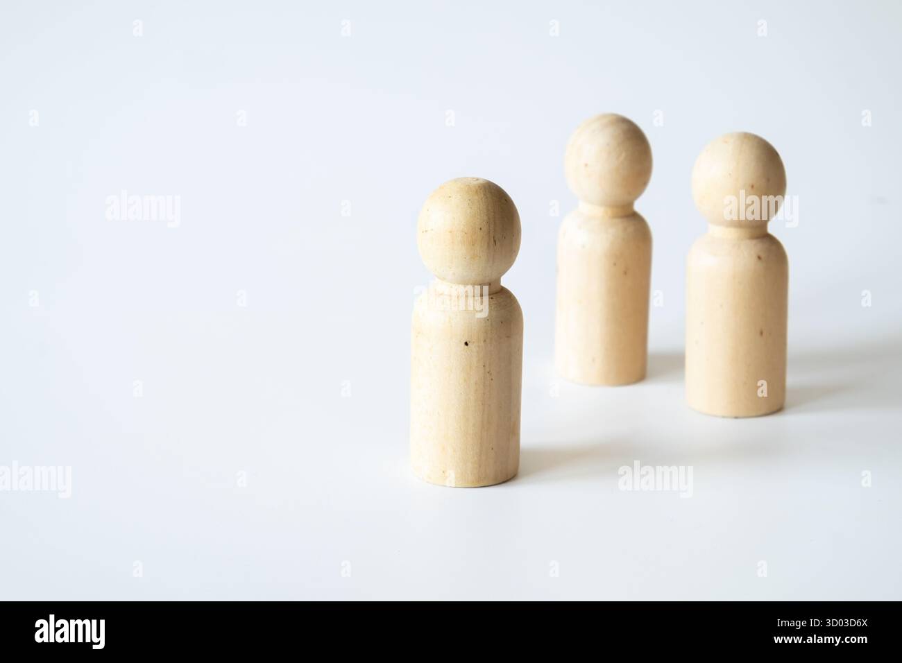 Tre semplici figure a piolo di legno in una disposizione triangolare su sfondo bianco, che rappresentano la semplicità e i concetti creativi nell'istruzione. Foto Stock