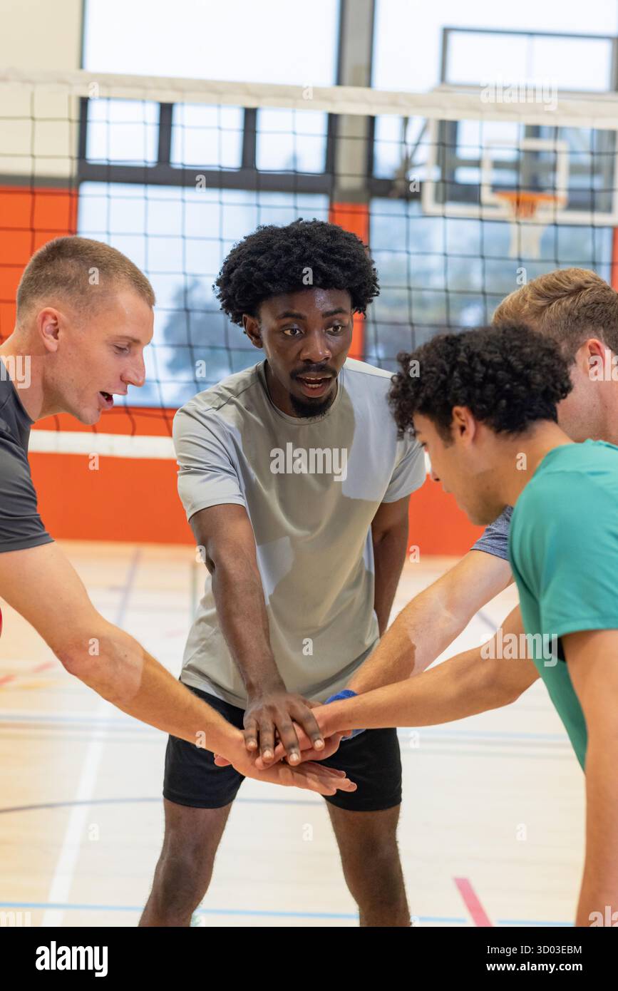 Diversi compagni di squadra maschili in equipaggiamento che si ammanettano e si impilano le mani sotto la rete da pallavolo sul campo con il cerchio. Lavoro di squadra, atletismo, sportività, ensemble, competitivo, fitness, dinamico || modello rilasciato Foto Stock