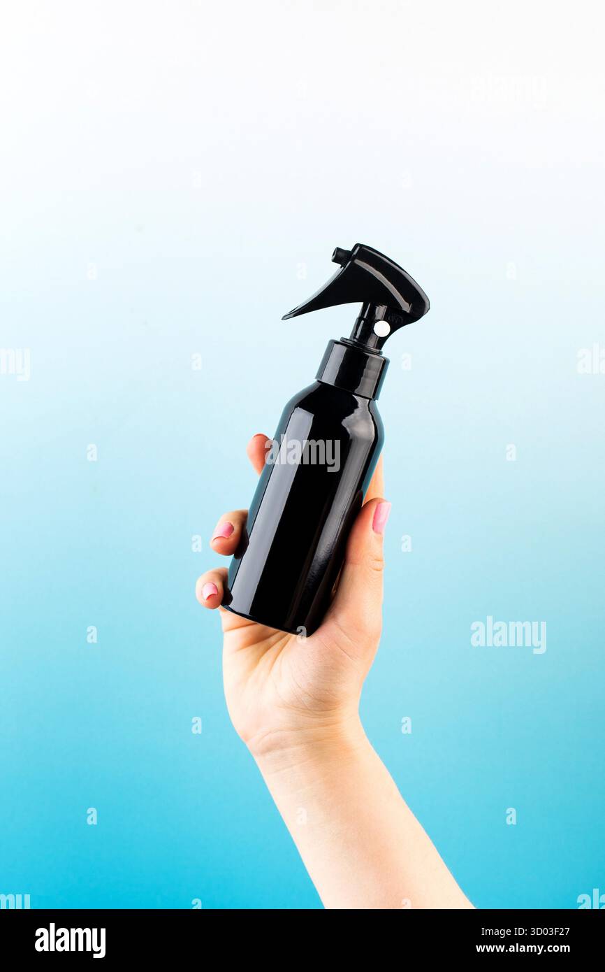 Un mockup di un prodotto professionale per capelli in un pulviliser marrone in una mano di una donna su uno sfondo blu. Spazio di copia. Foto Stock