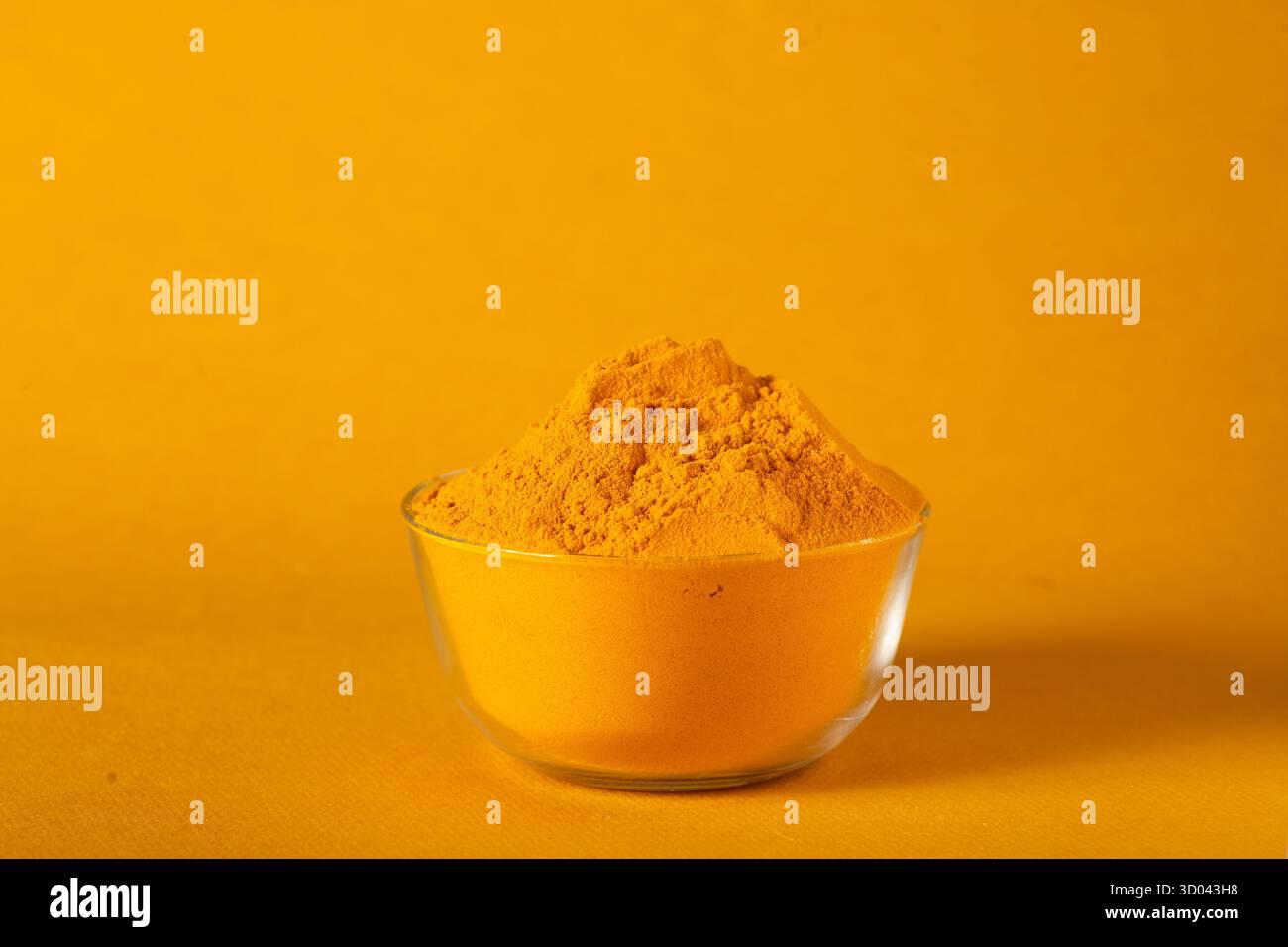 Polvere di curcuma in una ciotola di vetro su sfondo giallo, spezia tradizionale indiana utilizzata per cucinare e polvere di curcuma gialla AyurvedaVibrante, nota come Foto Stock