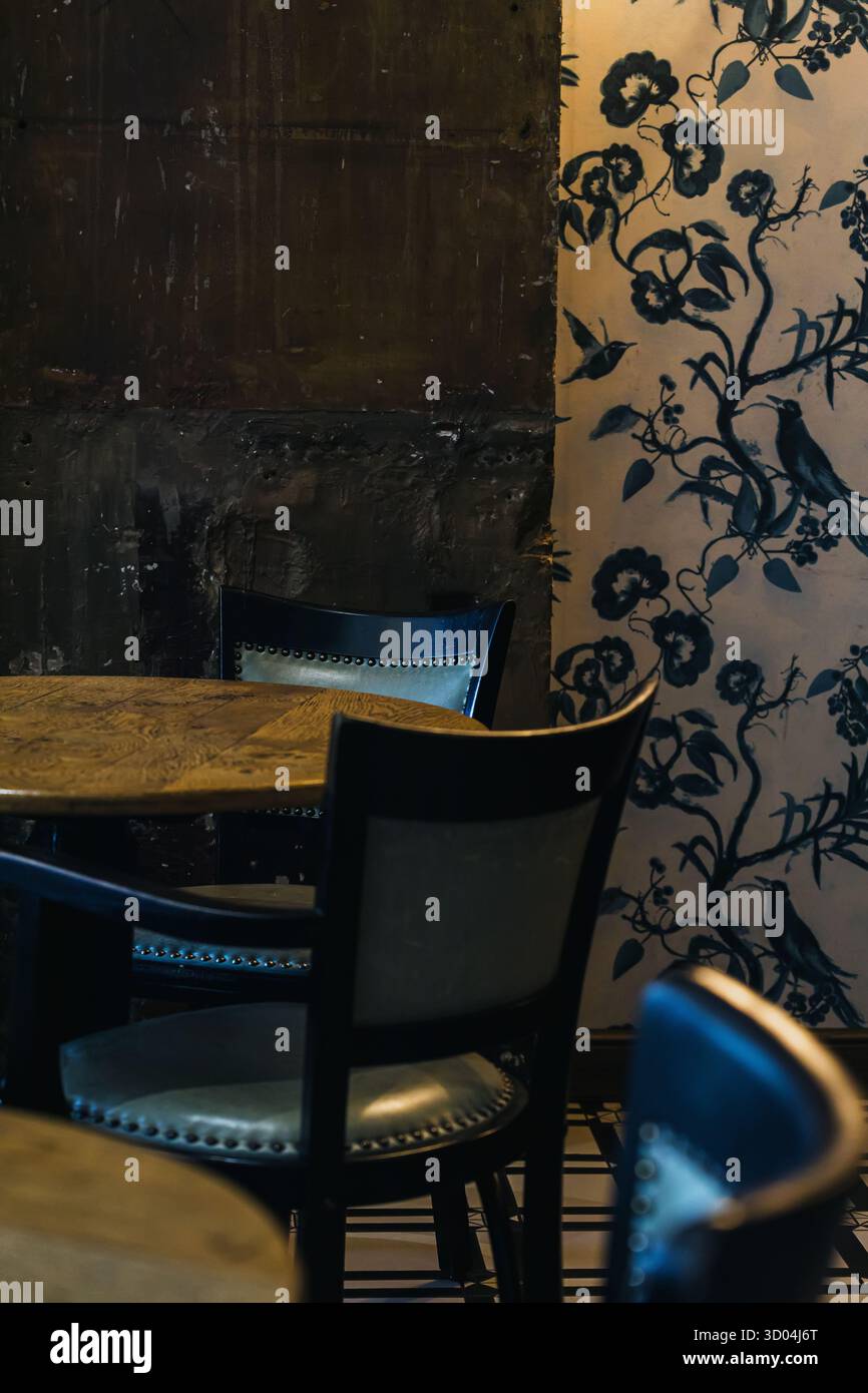 Un intimo ambiente da caffe' caratterizzato da un tavolo e sedie in legno sullo sfondo di intricate carte da parati floreali. Foto Stock