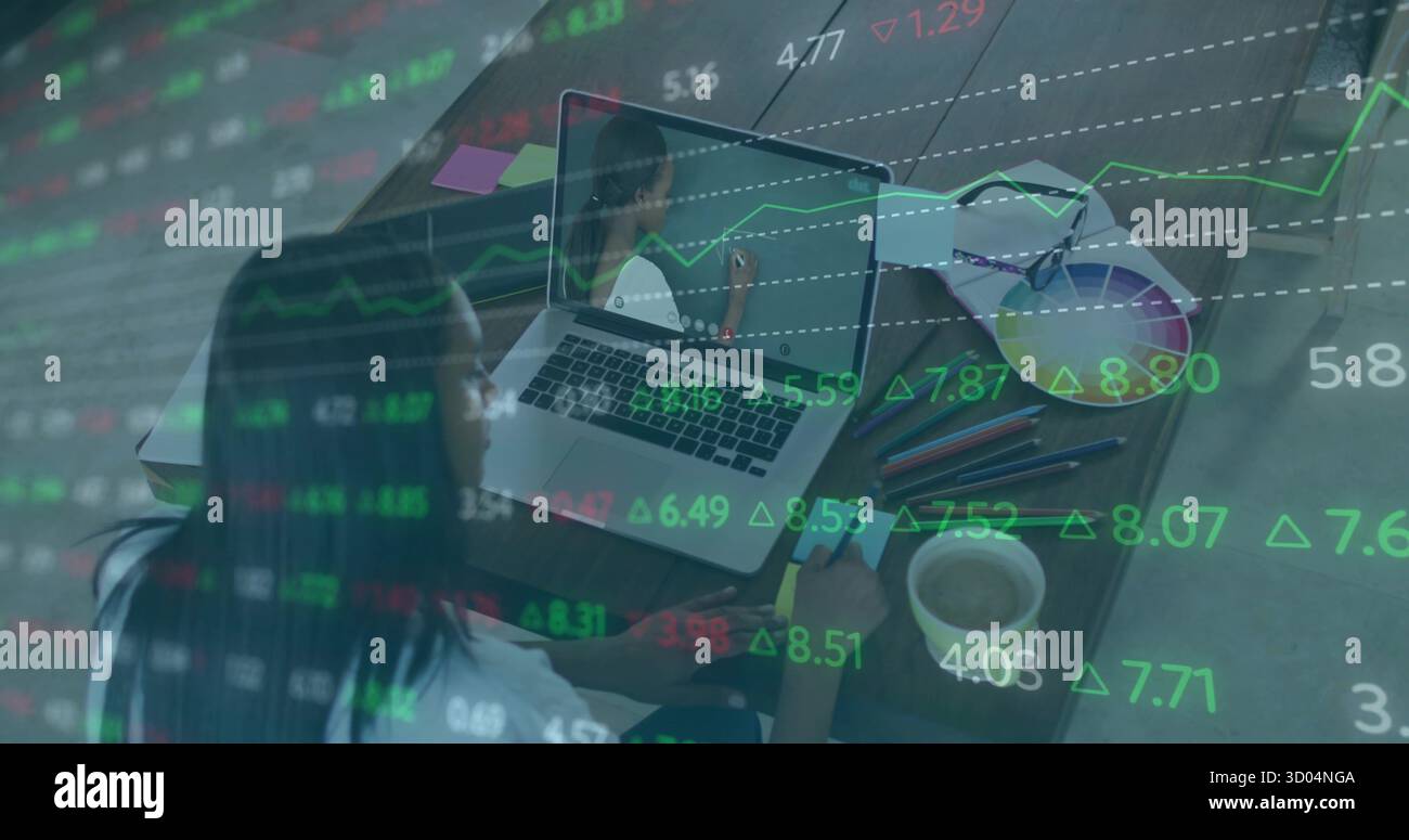 Analisi di grafici azionari donna afroamericana che prende appunti al portatile in ufficio domestico, con caffè Foto Stock