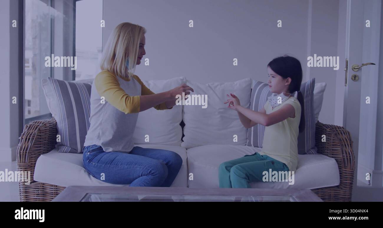 Madre e figlia che si scambiano maschera protettiva nella zona giorno della casa, con cuscini divano in vimini Foto Stock