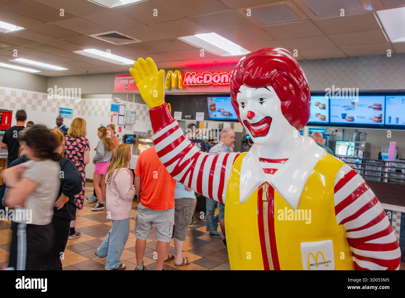 Ludlow, Massachusetts, Stati Uniti - 2 agosto 2025: Ronald McDonald in primo piano sventolando in un ristorante affollato nell'area di sosta dell'autostrada. Foto Stock