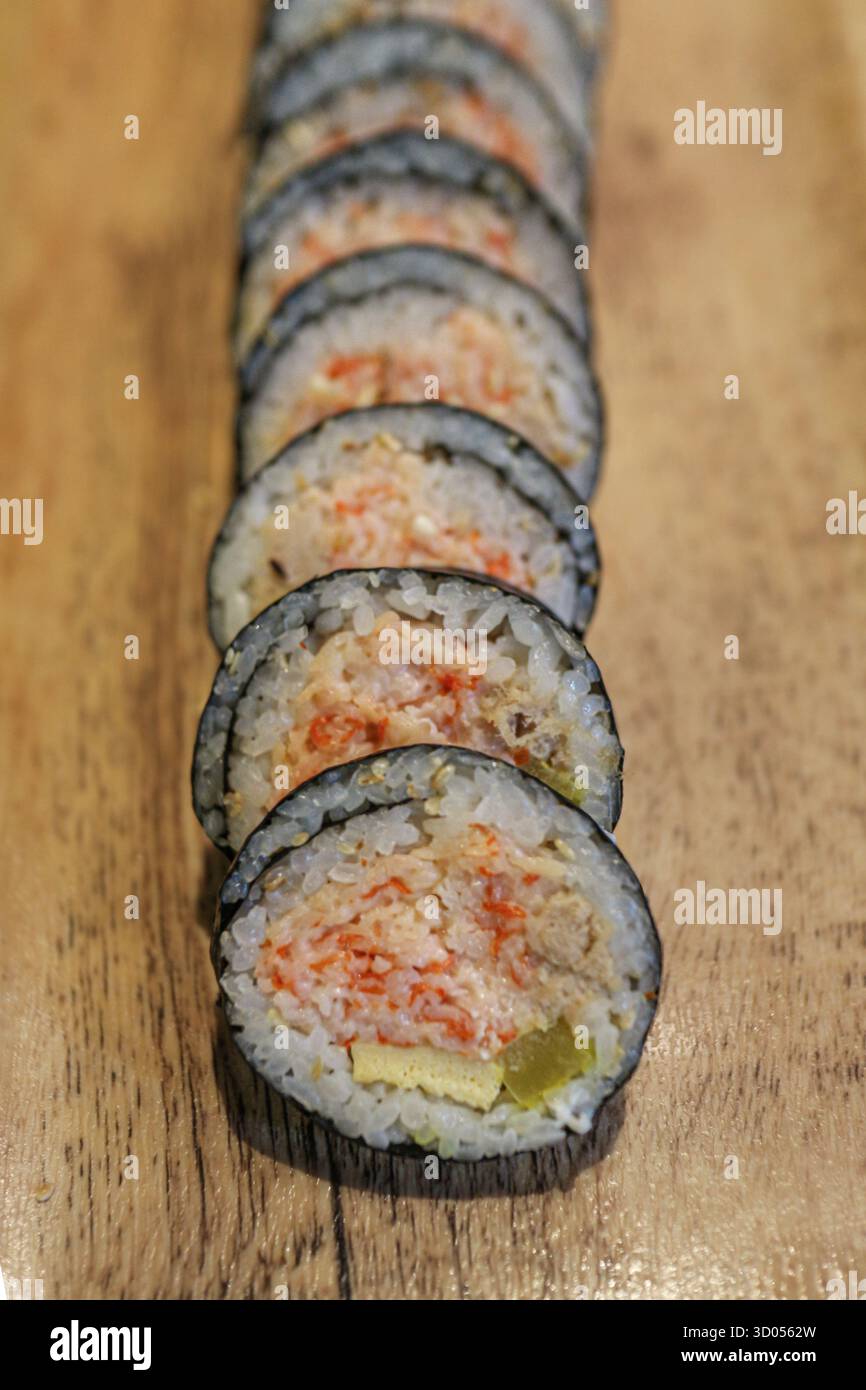 Kimbap coreano a fette ordinate (involtini di riso alle alghe) con ripieno di riso, tonno e bastoncini di granchio, servito su una tavola di legno. Un pranzo asiatico popolare e salutare. Foto Stock