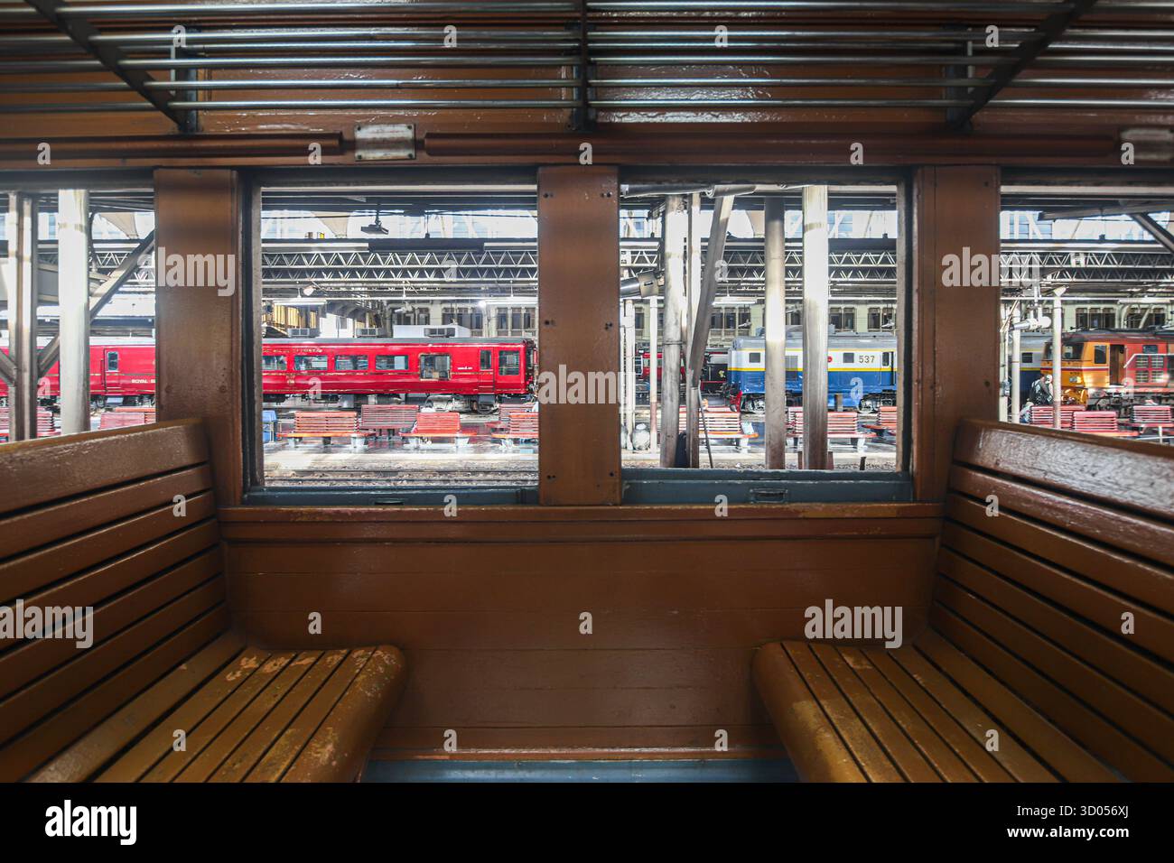 Interno di una carrozza ferroviaria tailandese in legno d'epoca con posti a sedere in legno lucido e finestre aperte, che mostra una colorata scena della stazione a Bangkok, Thailandia. Foto Stock