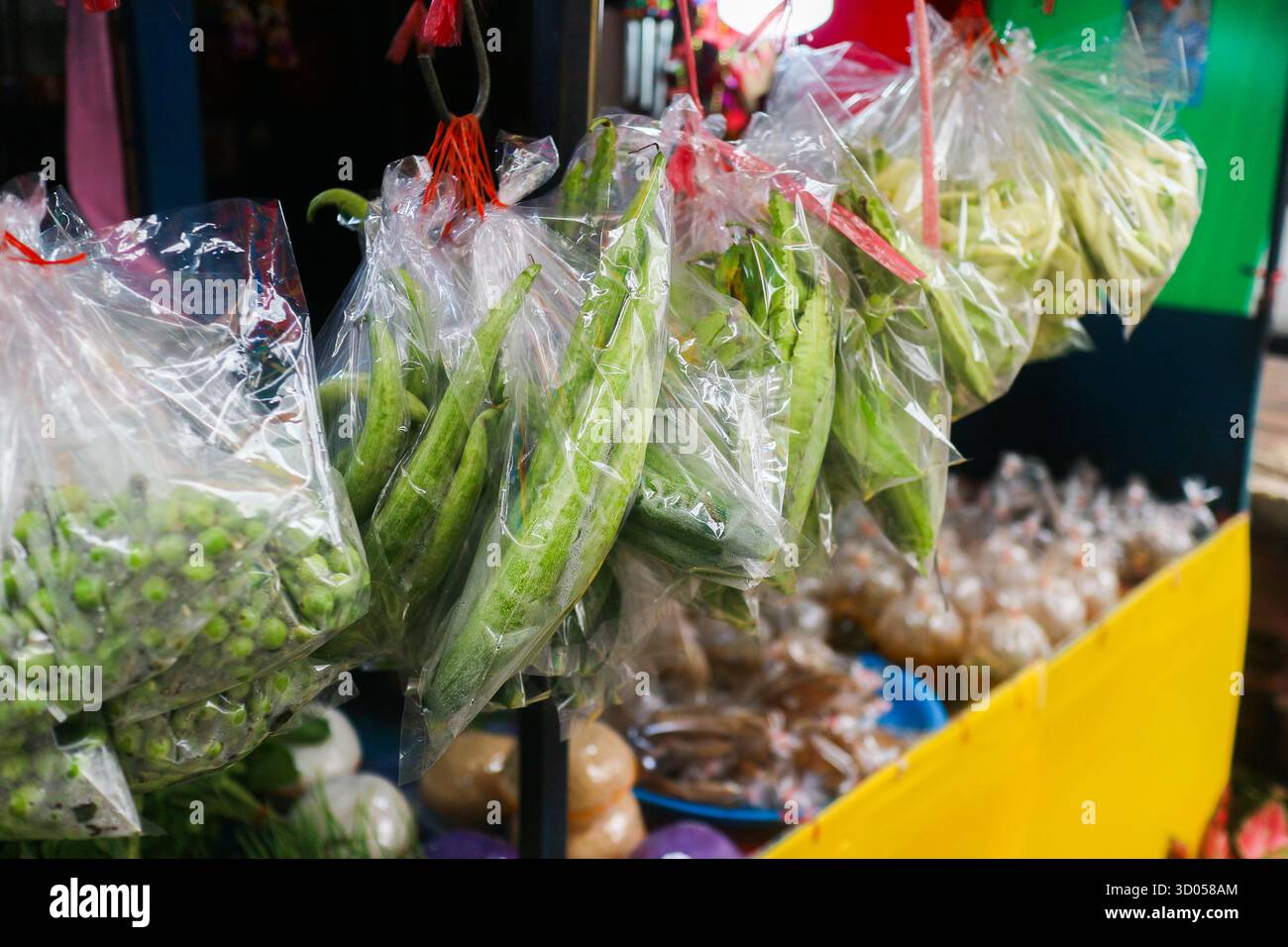 Prodotti asiatici freschi (Luffa, melanzana tailandese) appesi in sacchetti di plastica in un mercato. Cucina asiatica, cultura dei venditori ambulanti e rifiuti di plastica. Foto Stock