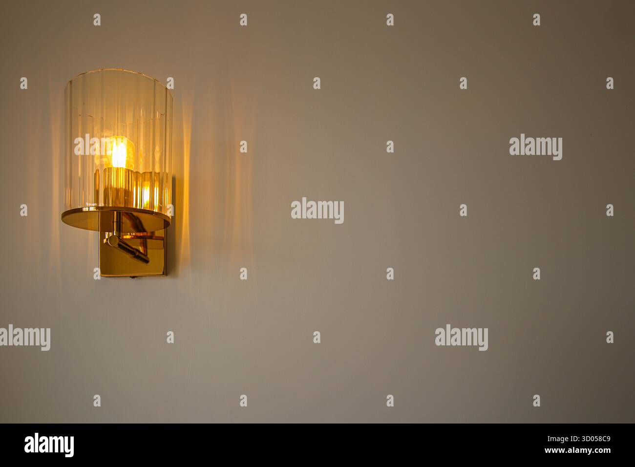 Applique minimalista in ottone che diffonde una luce calda su una parete pulita. Elemento di design per interni di lusso, ideale per l'arredamento della casa o lo sfondo dell'esposizione dei prodotti. Foto Stock