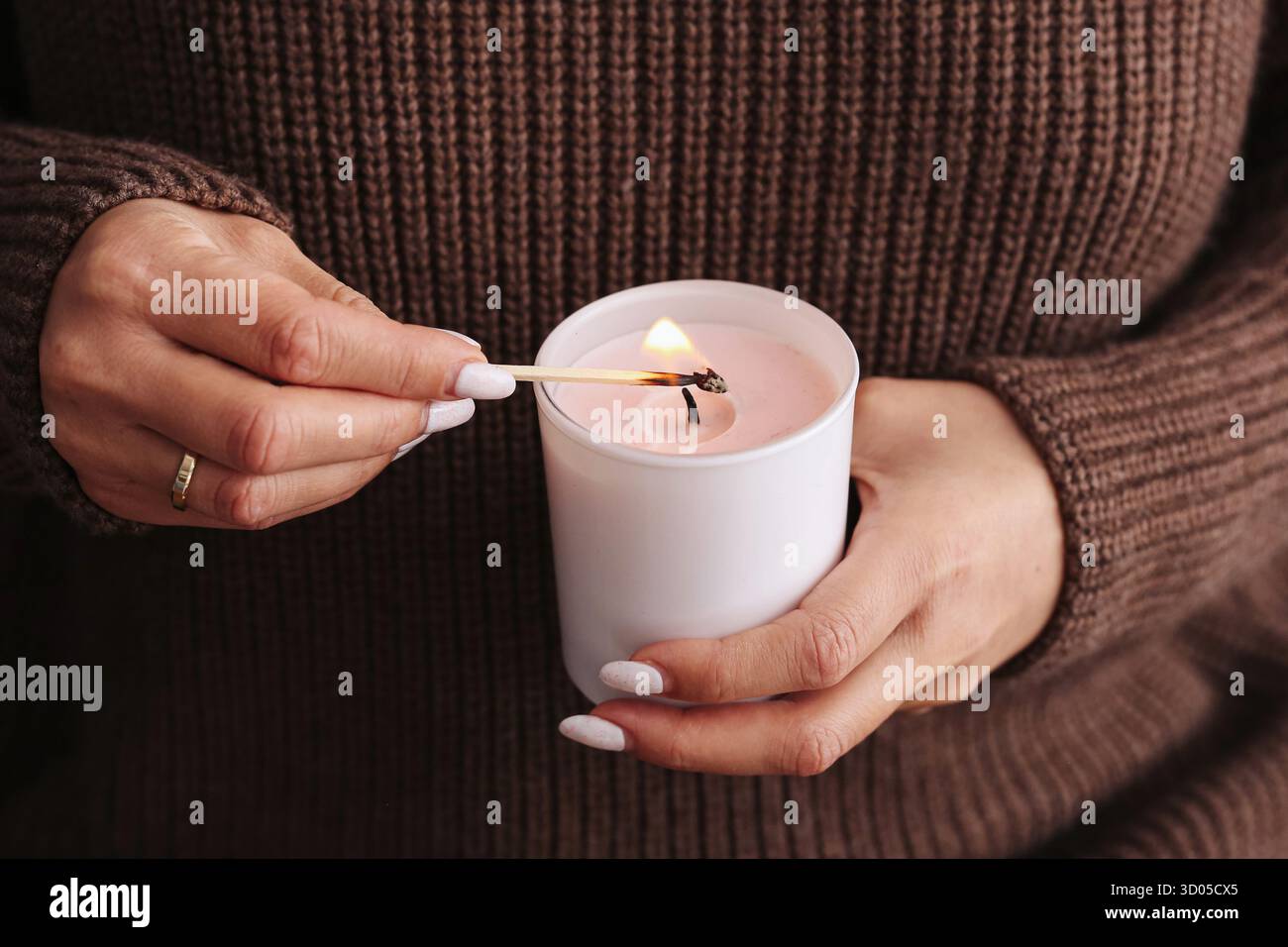 Donna che accende la candela con il fiammifero. Atmosfera accogliente e atmosfera rilassante. Concetto di comfort e cura personale. Foto Stock