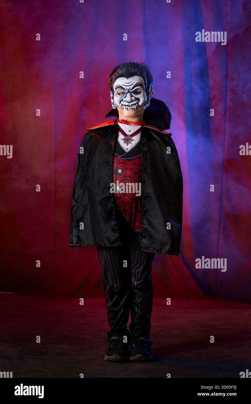 Ragazzo vestito con un costume da vampiro, con fumo colorato dietro di lui. Scena di Halloween. Foto Stock