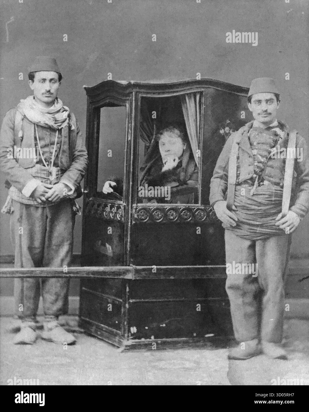 Due signori turchi in piedi accanto a una sedia berlina con una donna dentro Foto Stock