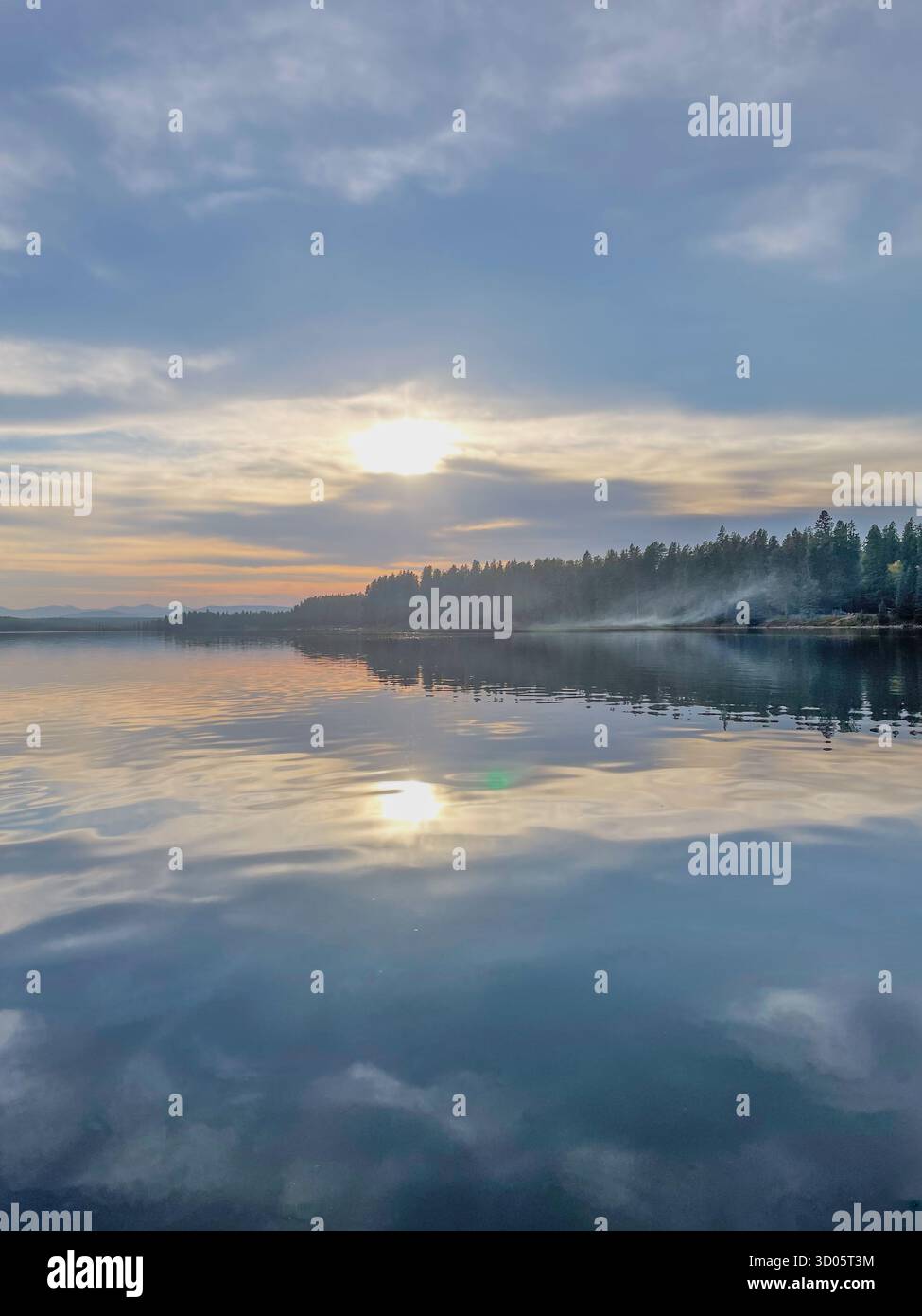 Un tranquillo tramonto su un lago calmo riflette il cielo e la foresta circostante. La morbida nebbia lungo la riva aggiunge un'atmosfera serena e naturale Foto Stock