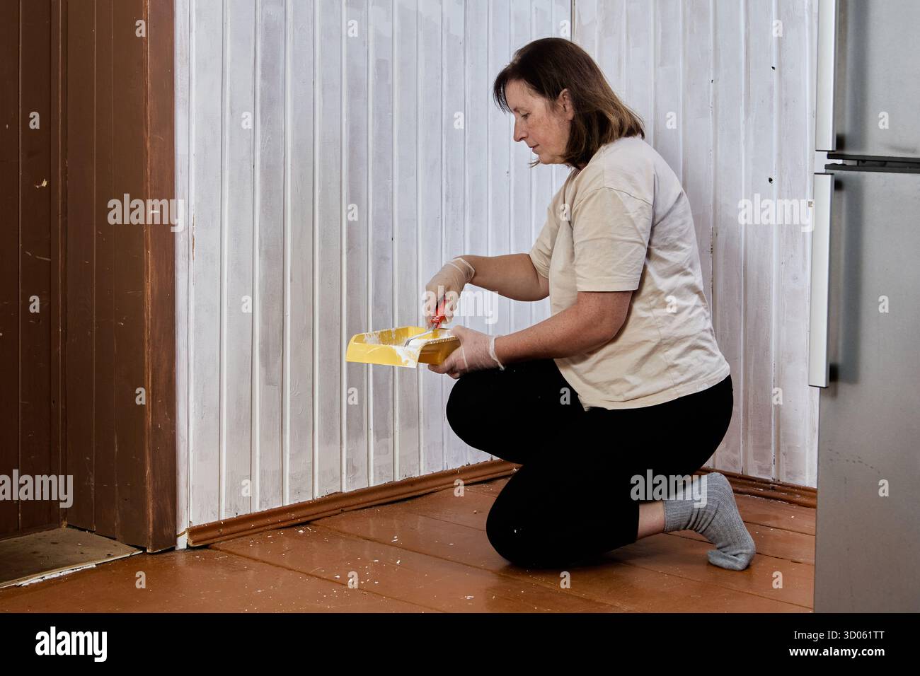 Lo strato iniziale di vernice sembra procedere lungo la carenatura della parete della linguetta e della scanalatura, il pittore si inginocchia sul pavimento e rotola la vernice bianca su verticale Foto Stock