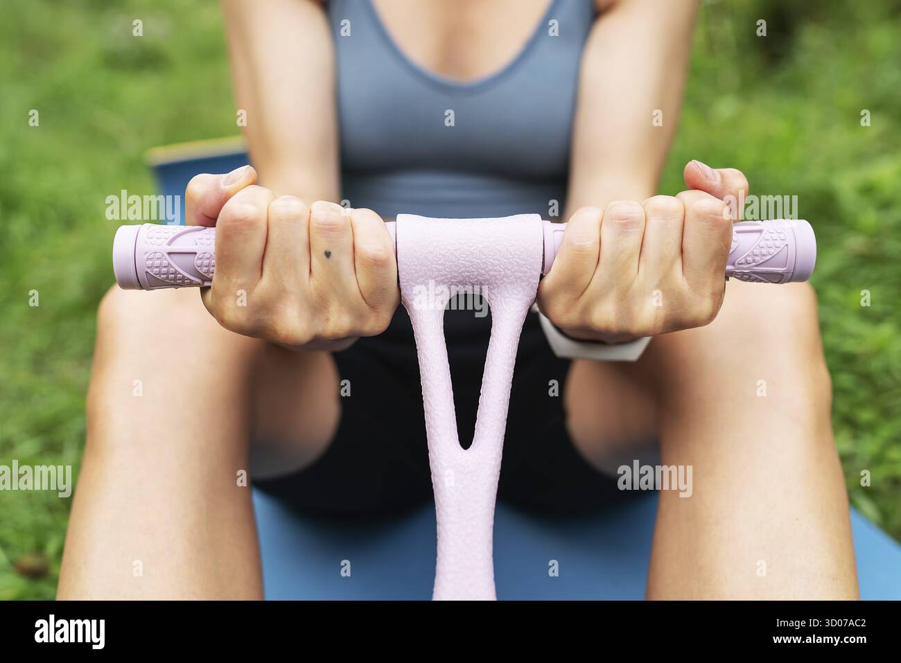 Ragazza atletica facendo esercizi su un allenatore a mano in natura all'aperto su uno sfondo sfocato. Una donna sta facendo yoga nel parco, seduta sull'erba Foto Stock