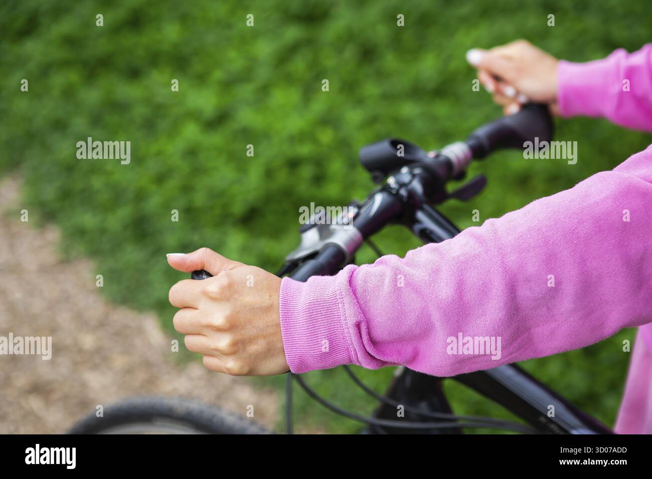 Una bambina in felpa rosa si tiene sul manubrio di una bicicletta, un giro in bicicletta nel parco. Le attività ricreative all'aperto sono buone per la salute Foto Stock