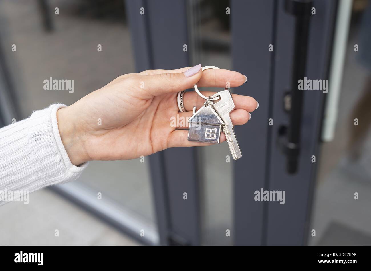 La mano di una donna apre la porta con una chiave su cui il portachiavi è appeso a casa e copia lo spazio Foto Stock