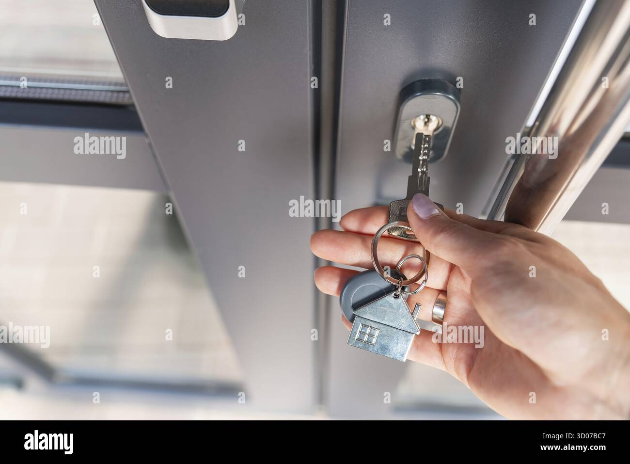 La mano di una donna apre la porta con una chiave su cui il portachiavi è appeso a casa Foto Stock