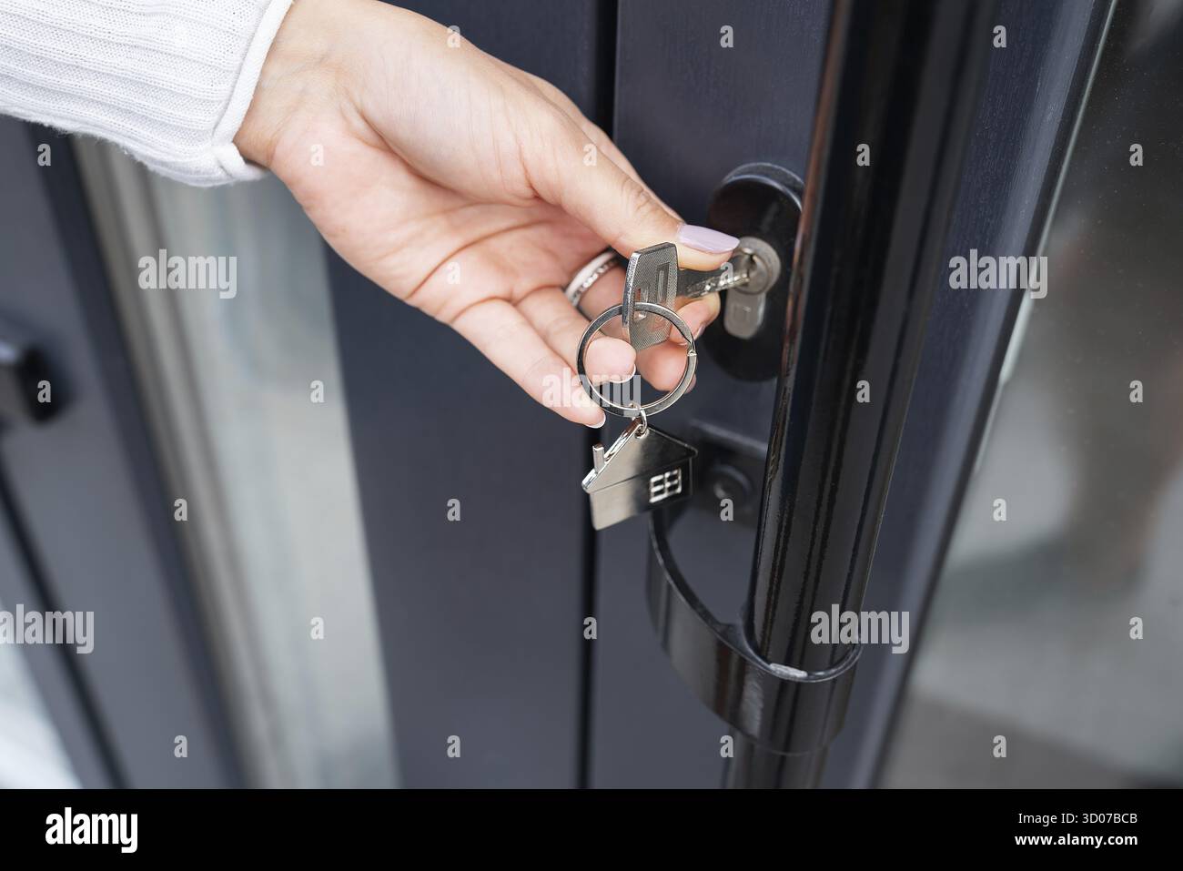 La mano di una donna apre la porta con una chiave su cui il portachiavi è appeso a casa e copia lo spazio Foto Stock