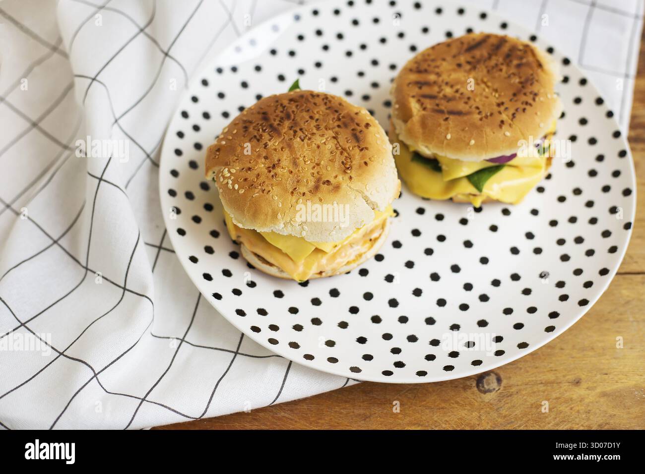 Hamburger grandi e gustosi si trovano su un piatto di piselli neri. Tavolo in legno e tovagliolo bianco a scacchi Foto Stock