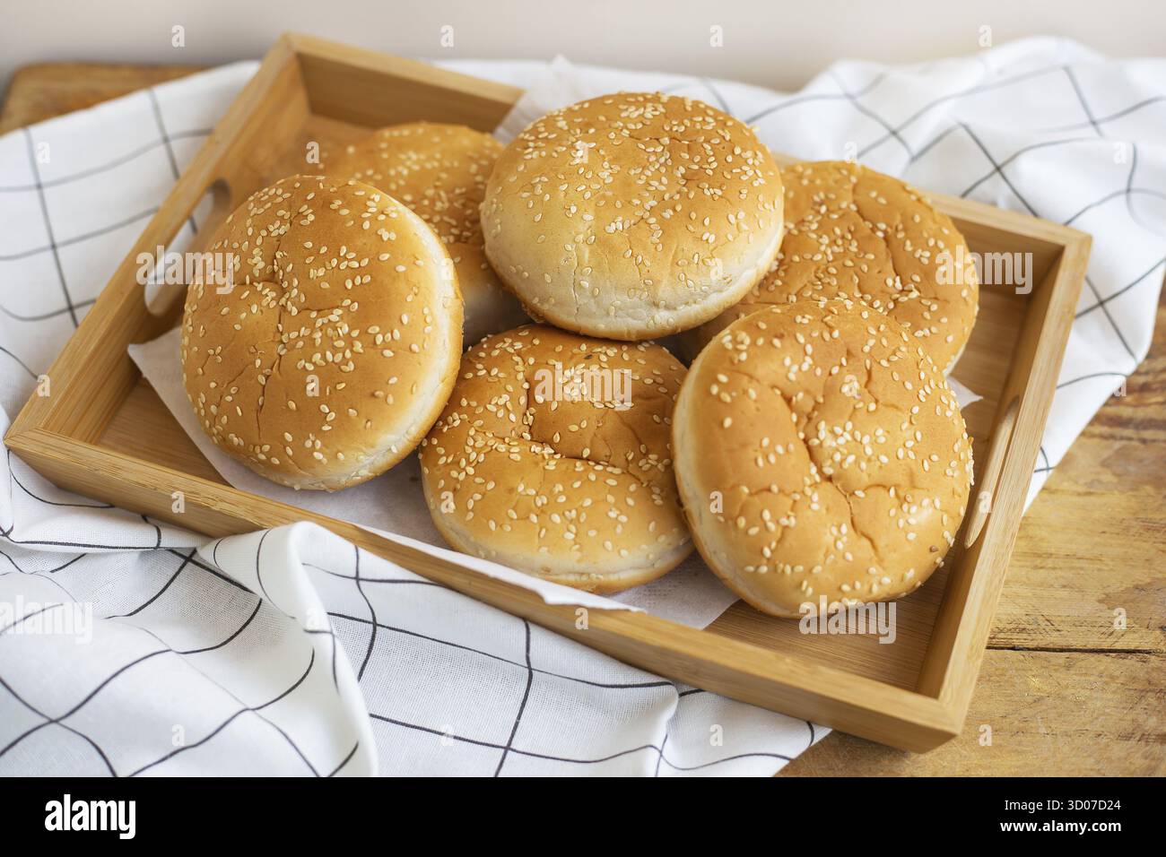 I panini appena sfornati si trovano su un vassoio di legno sul tavolo con un tovagliolo bianco Foto Stock