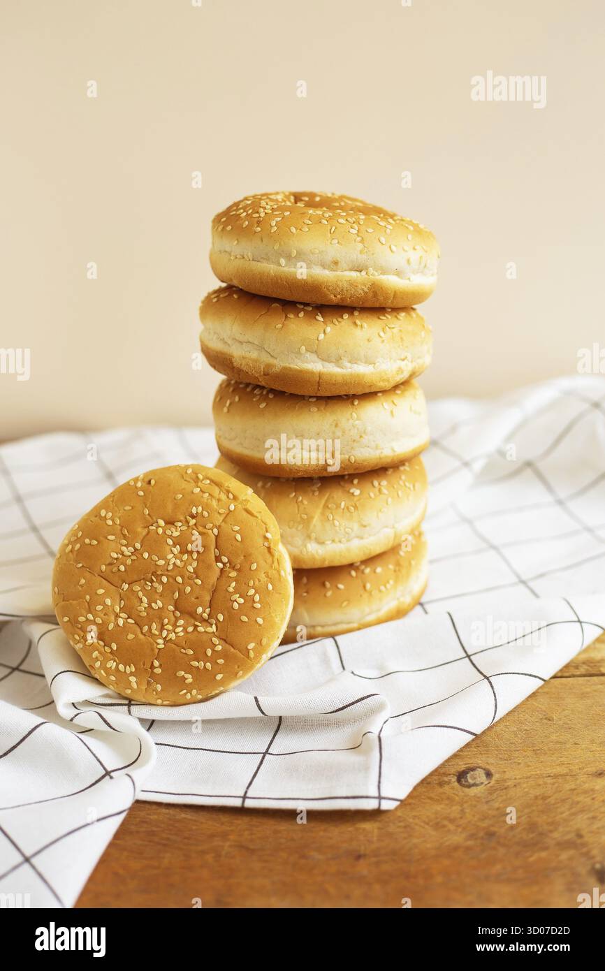 Magnifici panini appena sfornati per hamburger si trovano durati l'uno sull'altro sotto forma di torre su un tavolo di legno con un tovagliolo bianco a scacchi. Primo piano Foto Stock
