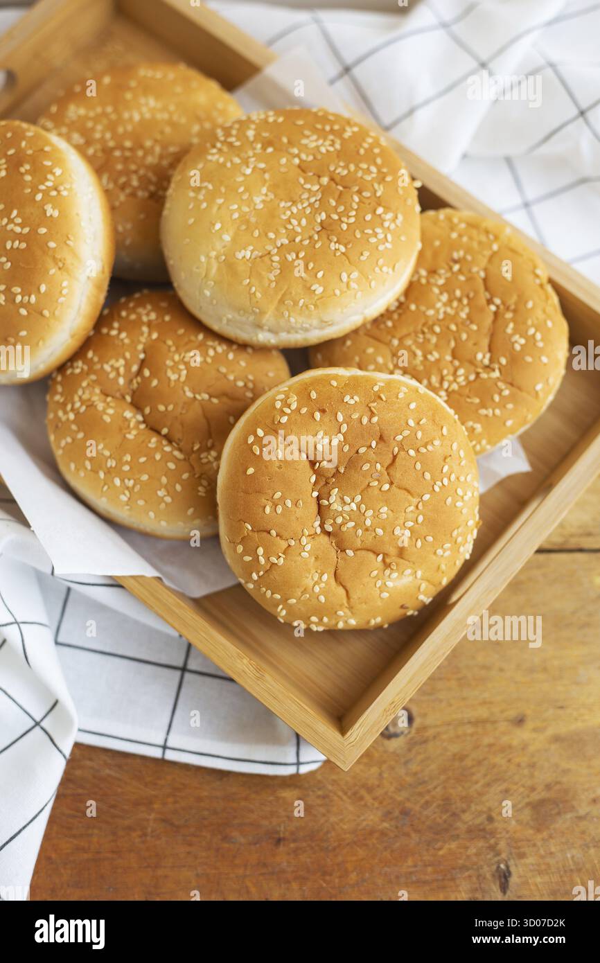 I panini appena sfornati si trovano su un vassoio di legno sul tavolo con un tovagliolo bianco. Dolci al gusto giallo con semi di sesamo bianchi Foto Stock