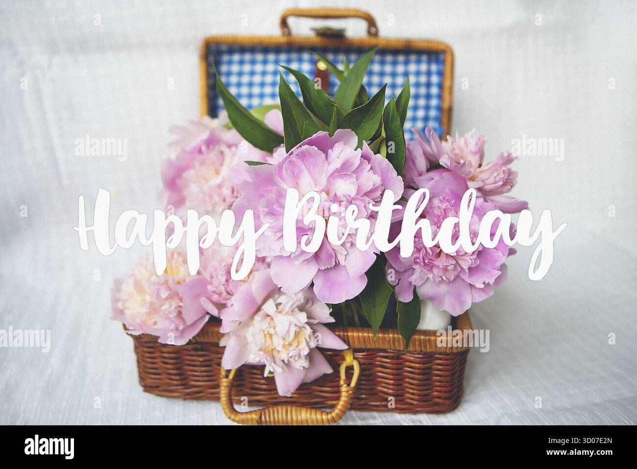Un bellissimo bouquet di peonie rosa in un vaso si erge su una valigia di legno. Bella composizione. Iscrizione buon compleanno Foto Stock