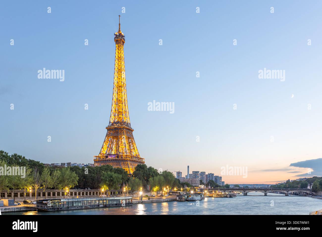 Veduta della Torre Eiffel illuminata che perfora il cielo crepuscolo, il suo bagliore dorato che si riflette sulla Senna, foto di terra, Parigi, Île-de-France, Francia. Foto Stock