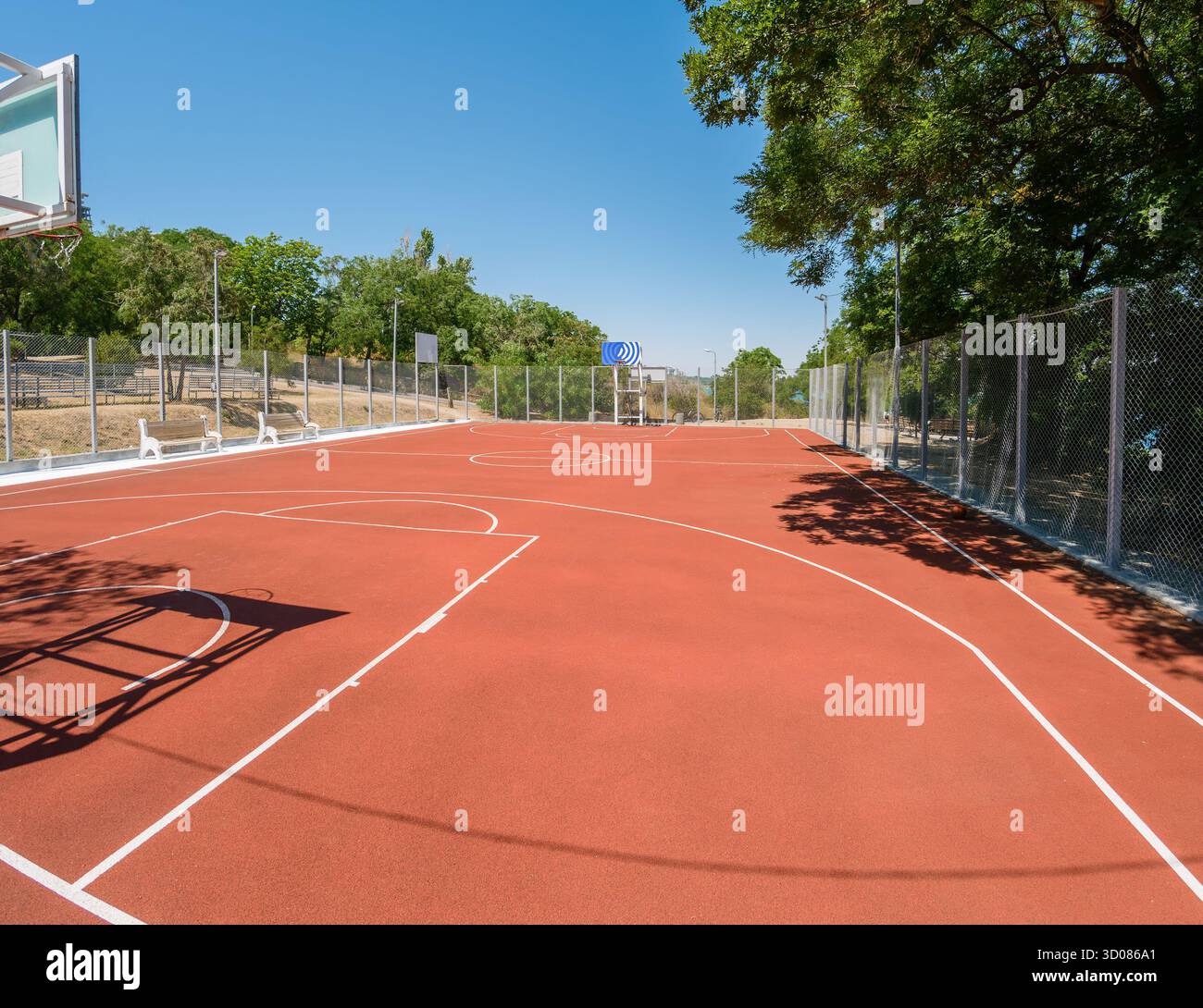 Un campo da pallacanestro all'aperto inondato dalla luce del sole nelle giornate limpide, perfetto per sport, esercizio fisico e attività ricreative sotto il cielo azzurro Foto Stock