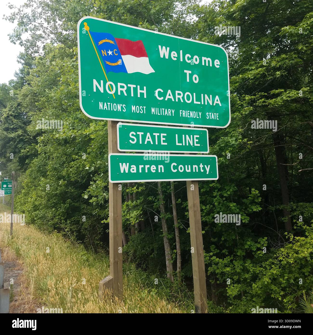 Benvenuto al cartello della North Carolina State Line con la bandiera dello stato e lo slogan "Stato più amichevole della nazione" nella lussureggiante foresta della contea di Warren Foto Stock