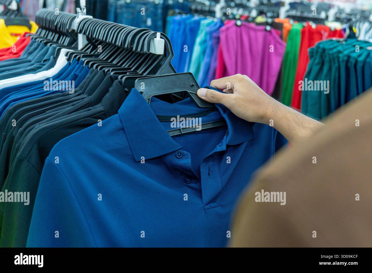 Primo piano di una persona che sceglie una polo blu da un appendiabiti in un negozio. Concetto di moda, shopping, vendita al dettaglio e scelta dei consumatori. Foto Stock