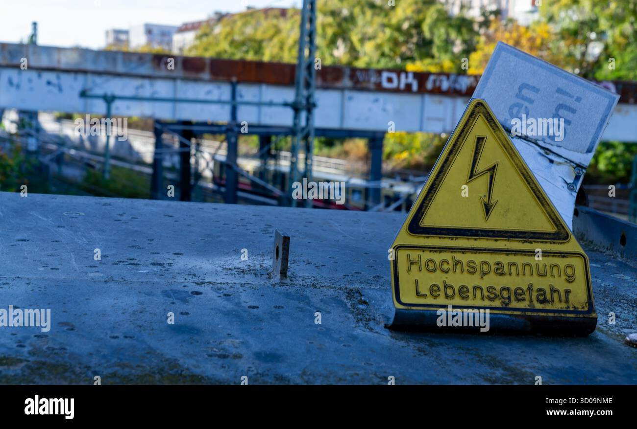 Segnale di avvertimento giallo triangolare tedesco "pericolo di morte ad alta tensione" (Hochspannung Lebensgefahr) su un ponte ferroviario a Berlino Prenzlauer Berg. Foto Stock