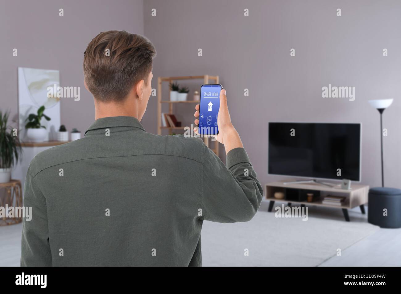 Uomo che utilizza l'app Smart Home sul telefono cellulare per controllare le funzioni della casa Foto Stock