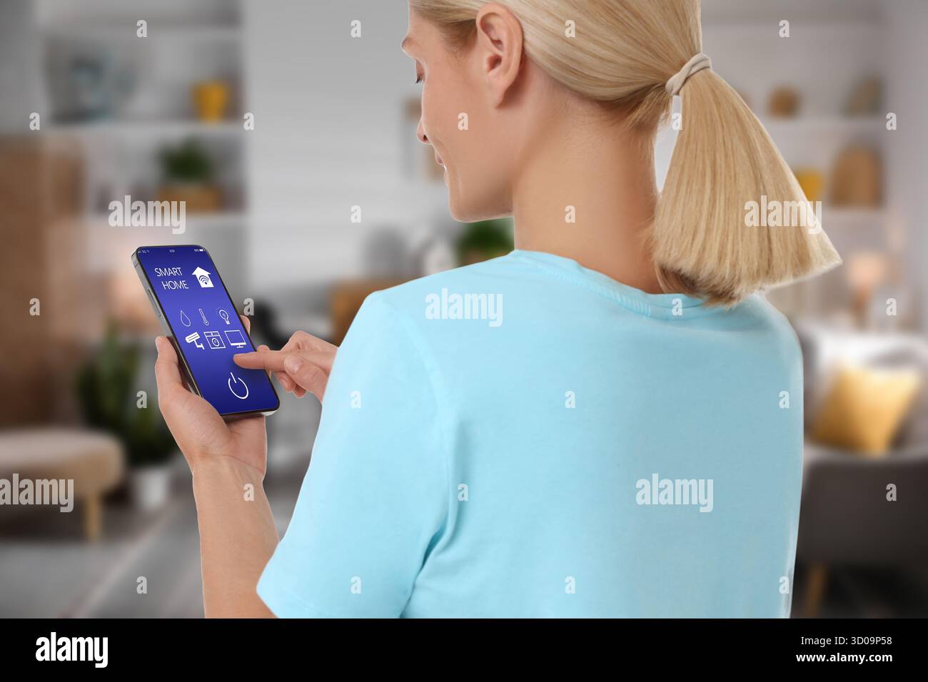 Donna che utilizza un'app per la casa intelligente sul telefono cellulare per controllare le funzioni della casa Foto Stock