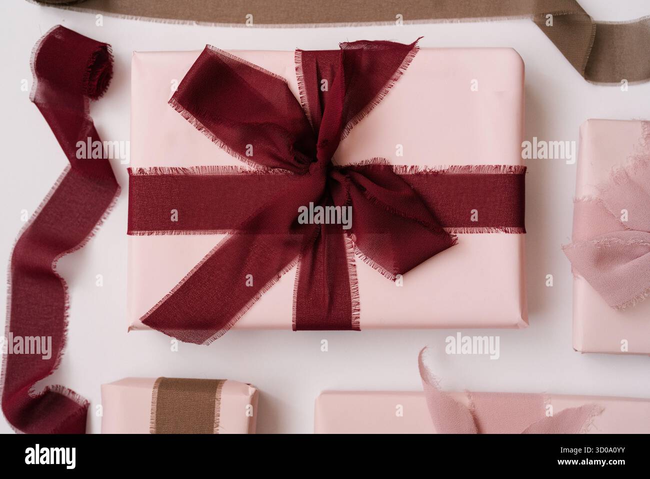 Modello piatto di eleganti confezioni regalo rosa, confezionate con morbidi nastri in tessuto in tonalità Bordeaux e rosa polverosa su sfondo bianco. Estetica minimalista Foto Stock